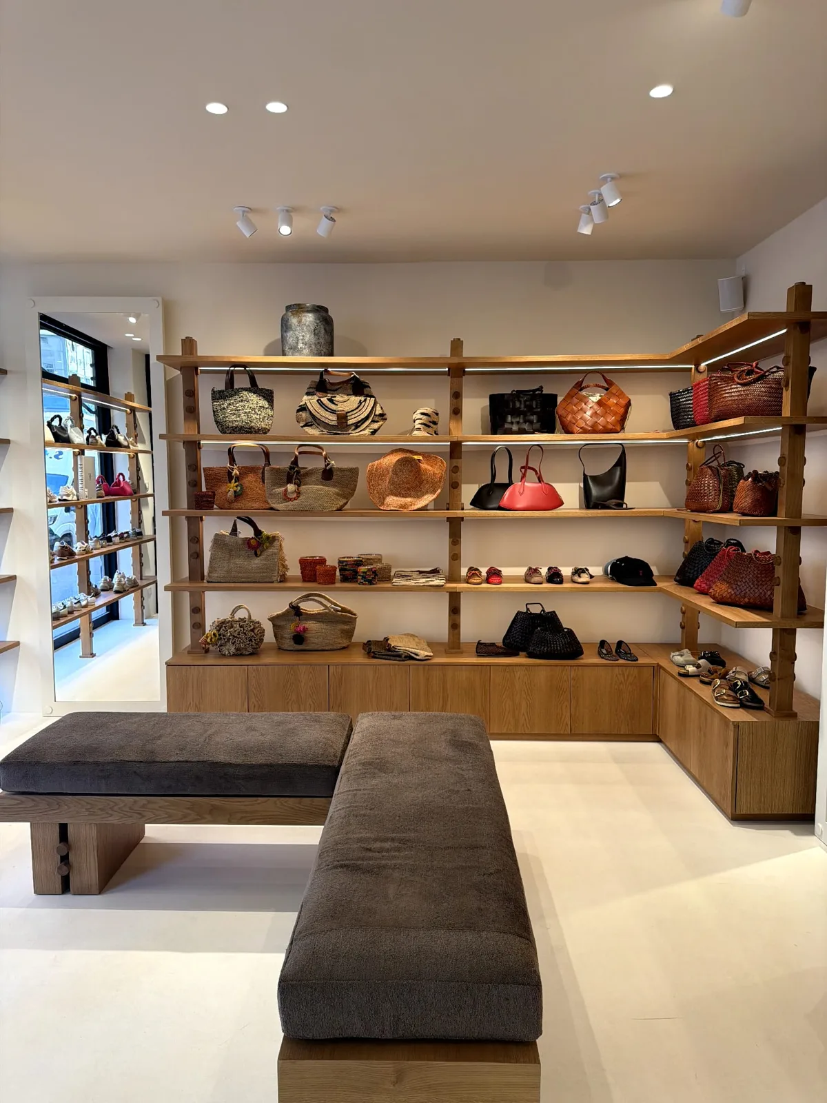 Wall of designer bags, hats and small accessories on wooden shelves in a Lulli boutique